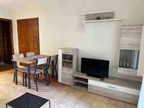 A compact living space with a dining table, chairs, a TV, and a small cabinet. - Beachfront Apartment in Denia (Denia)
