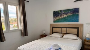 A bedroom with a bed, a nightstand, a lamp, a painting, and a window with curtains.