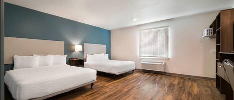Ein Hotelzimmer mit zwei Betten, einem Nachttisch, einer Lampe, einem Fenster mit Jalousien, einem Heizkörper und einem Kleiderschrank.