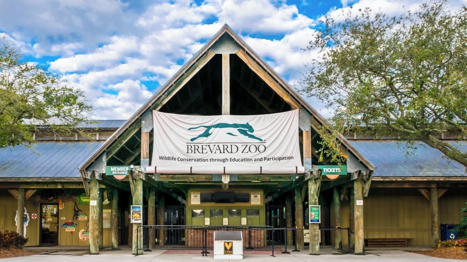 L’entrée du zoo de Brevard, avec une grande banderole, un guichet de vente de billets et des panneaux d’information pour les visiteurs.