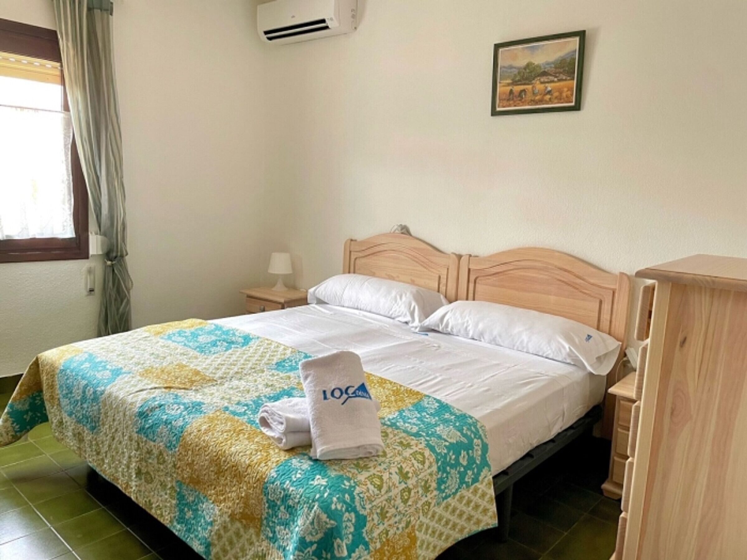Une chambre d’hôtel avec un lit, une table de chevet, une lampe, un tableau au mur et une fenêtre avec des rideaux.
