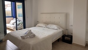 A bedroom with a bed, a nightstand, a window with a view, and a door leading to an outdoor area. - Modern apartment in Denia, 2 bedrooms, beachfront (Denia)