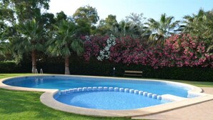 A swimming pool with a curved edge, surrounded by well-maintained grass and palm trees. - Modern apartment in Denia, 2 bedrooms, beachfront (Denia)