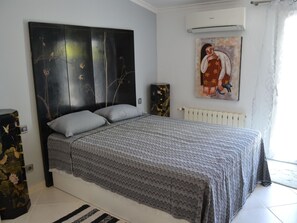 A bedroom with a bed, a radiator, a painting, and a window.