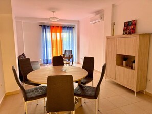 A dining area with a round table, six chairs, a cabinet, and a window with curtains.