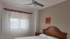 Hotellihuone, jossa on sänky, yöpöytä, kattotuuletin, ikkuna verhoilla ja seinälle kiinnitetty taideteos.