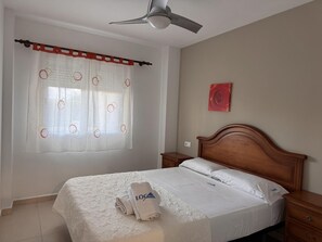 A hotel room with a bed, a nightstand, a ceiling fan, a window with curtains, and a wall-mounted artwork. - Seaside apartment in Denia with pet-friendly, parking and air conditioning (Denia)