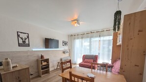 Un accogliente soggiorno con un tavolo da pranzo in legno, un comodo divano rosso, una TV a parete e un'ampia finestra con tende leggere.