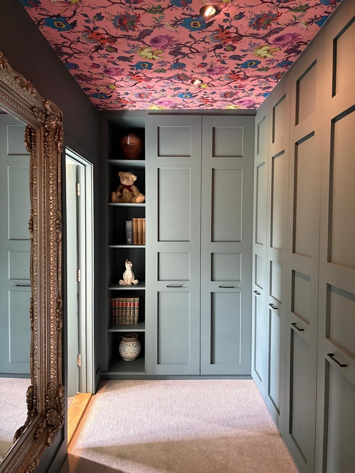 Un pasillo con techo floral, un espejo grande y un estrecho estante con objetos decorativos.