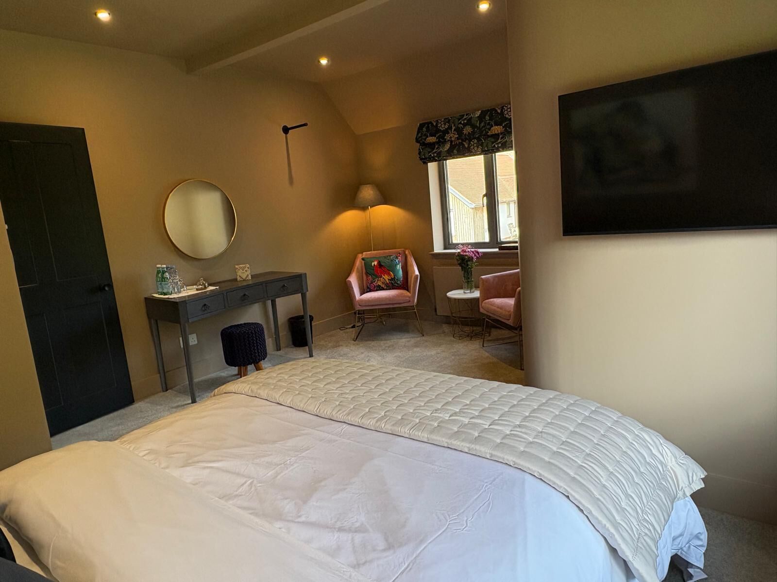 Une chambre avec un grand lit, un bureau, une chaise, une lampe et une fenêtre.