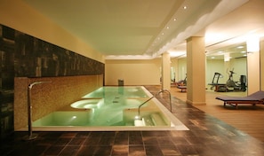 A spa area with a large hot tub, exercise equipment, and a wooden floor.