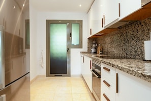 A modern kitchen with a granite countertop, stainless steel appliances, and a frosted glass door.