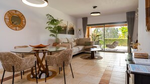 A modern living room with a round glass table, beige sofa, and a dining area with chairs. - Benatalaya golf views by Time & Home (Benahavís)