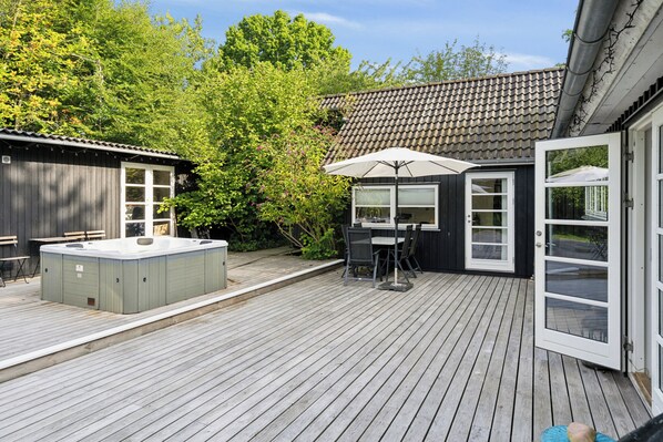A wooden deck with a hot tub, outdoor seating, and a covered area with a table and chairs.