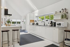 A modern kitchen with white cabinets, a black countertop, and a window overlooking greenery. - Modern house with outdoor spa and sauna (Faxe Ladeplads)