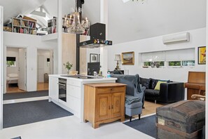 A spacious living area with a kitchen, a sofa, a wooden cabinet, and a large window.