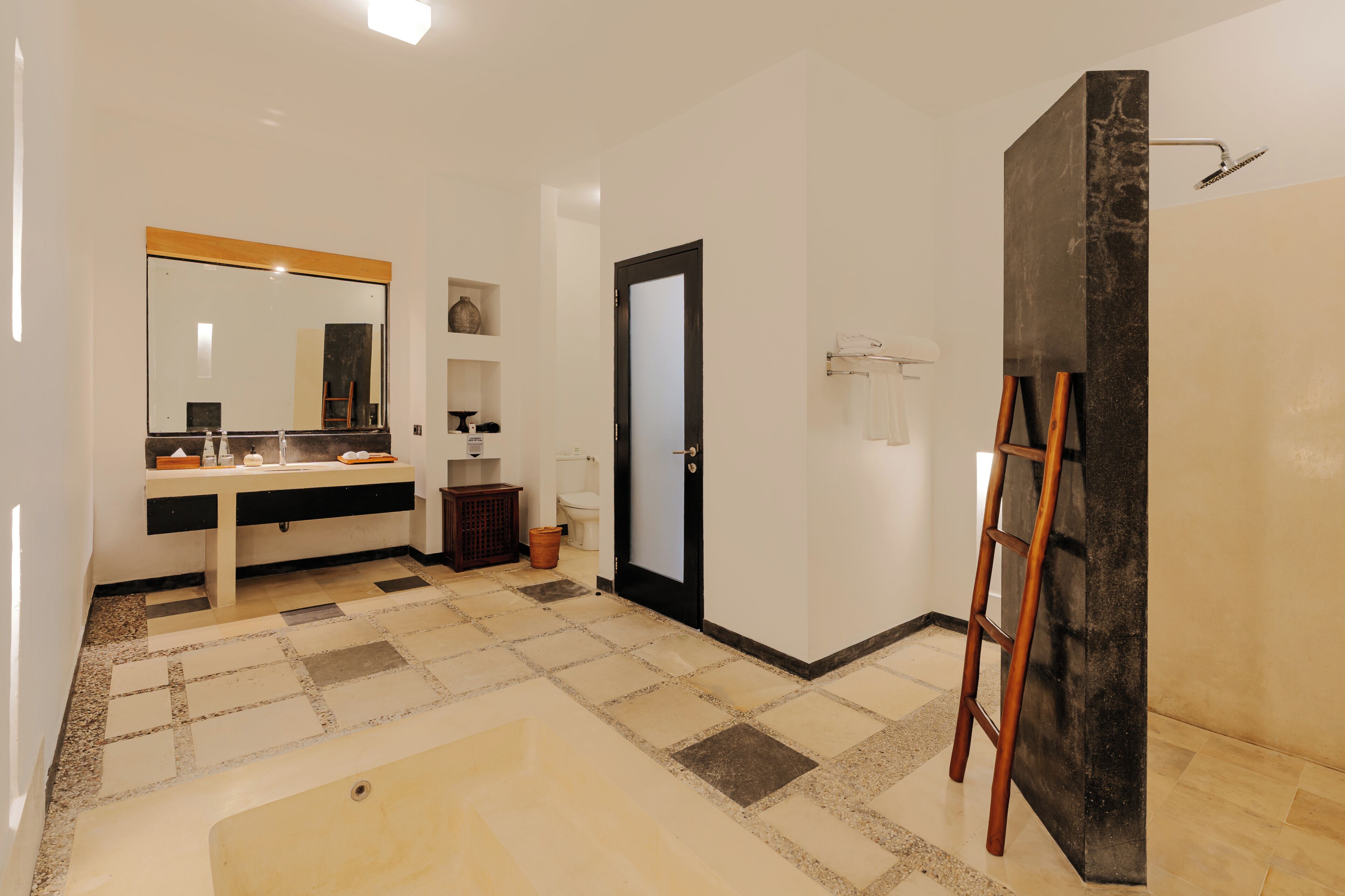 A bathroom with a large mirror, a sink, a toilet, a shower area, and a ladder leaning against a wall.
