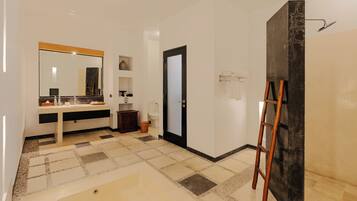 A bathroom with a large mirror, a sink, a toilet, a shower area, and a ladder leaning against a wall.