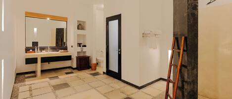 A bathroom with a large mirror, a sink, a toilet, a shower area, and a ladder leaning against a wall.