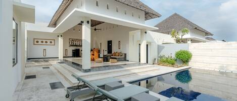 A modern house with a swimming pool, outdoor seating, and a covered patio area.