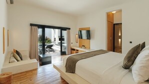 A modern hotel room with a large bed, a desk, a flat-screen TV, and a balcony with outdoor seating. - The Seminyak Suites Private Villas  (Seminyak)