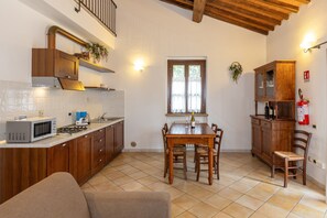 Una cocina con armarios de madera, una mesa de comedor con sillas, un microondas y una ventana con cortinas.