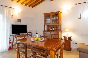 Un coin repas comprenant une table en bois, des chaises, un téléviseur, un meuble et une assiette de fruits.
