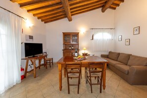Un coin repas avec une table et des chaises en bois, un téléviseur, un meuble avec des portes en verre et un canapé.
