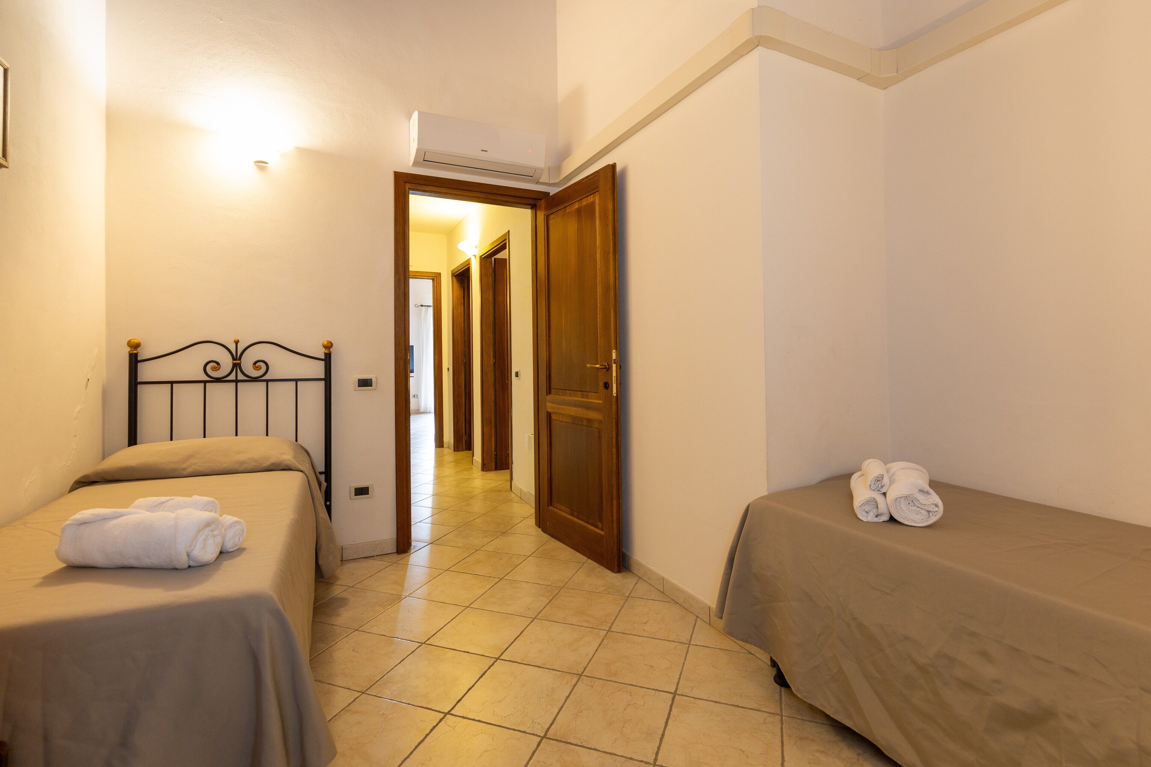 A hotel room with two beds, a wooden door, and a hallway leading to another room.