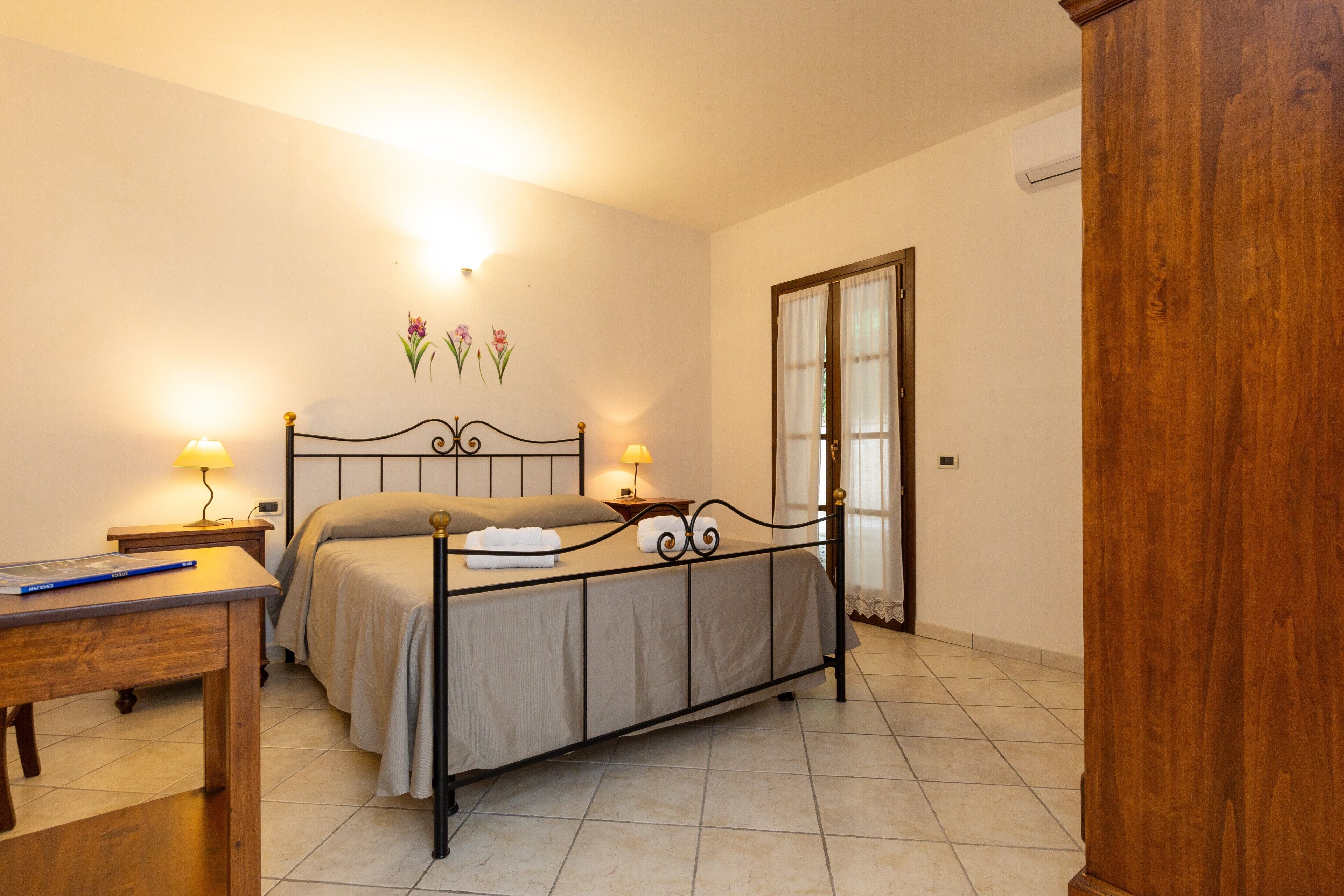 A bedroom with a bed, bedside lamps, a wooden desk, and a wardrobe.
