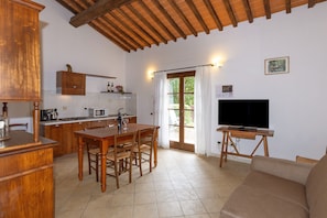 Una cucina con mobili in legno, un tavolo da pranzo e sedie. C'è una televisione su un mobile e un divano nella zona soggiorno.