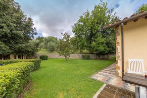 A well-maintained garden with a patio area, stone wall, and a white chair.