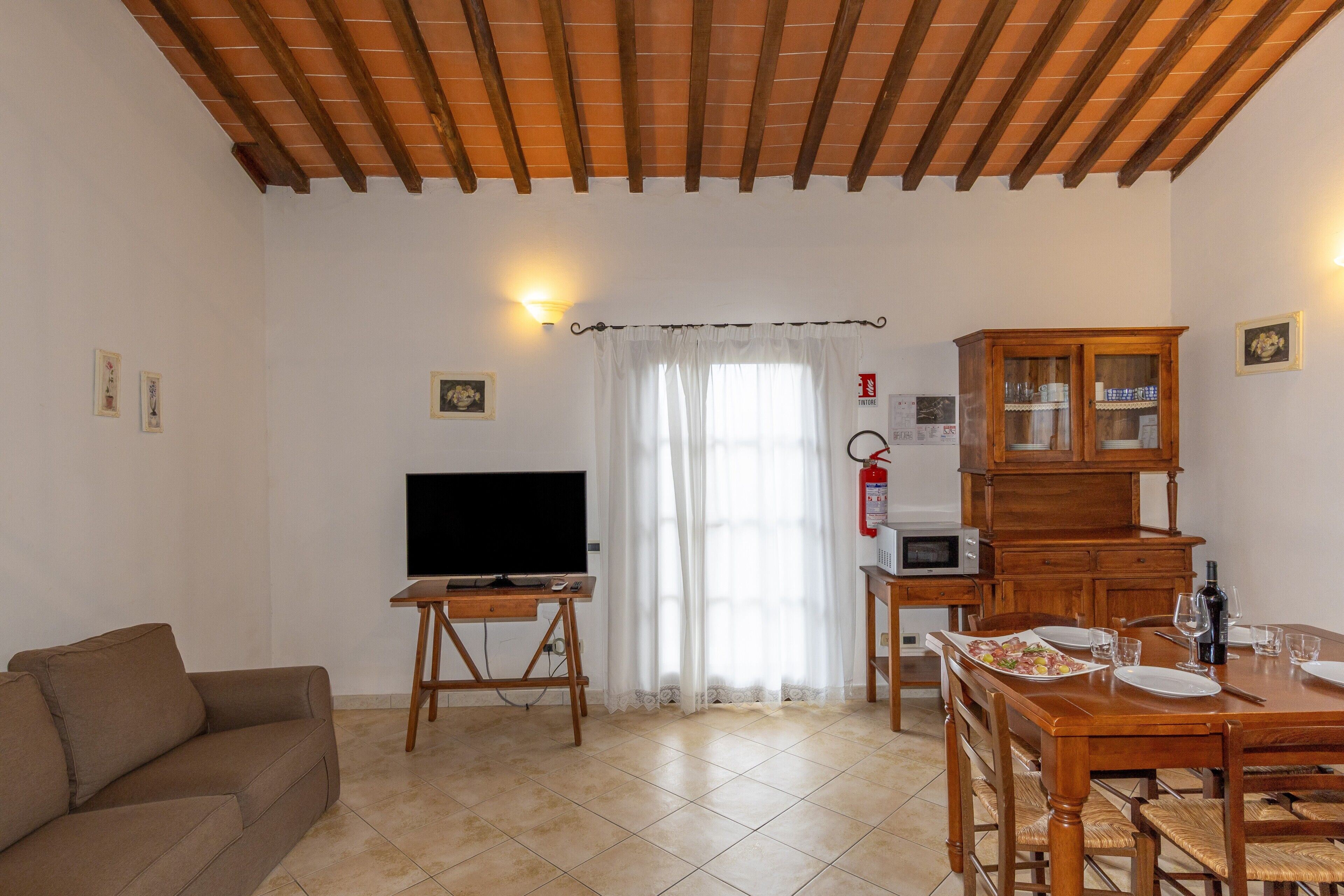 A living room with a television, wooden furniture, a dining table, and a kitchen area.