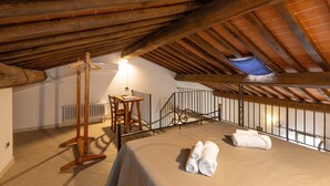 An attic bedroom with a sloped ceiling, a wooden chair, a small table, a bed with rolled towels, and a view through a window. - Apartment 'Biancospino' with Shared Pool, Wi-Fi, and Air Conditioning (Santa luce)