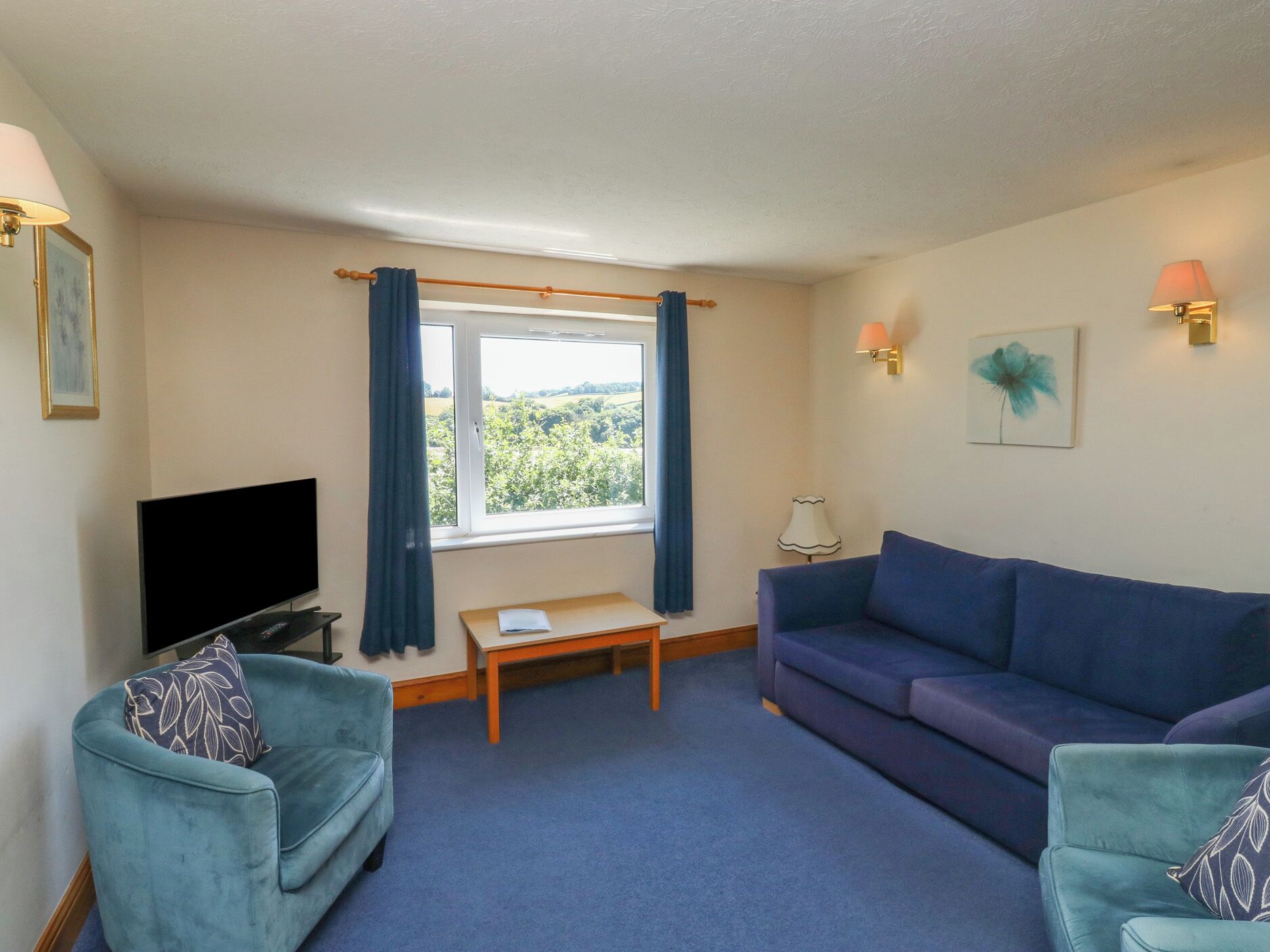 A living room with a TV, two sofas, a small table, and a window with curtains.