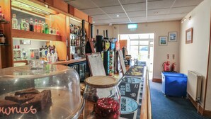 Eine Bar mit einer Auswahl an Spirituosenflaschen, einer Theke mit einem Glasbehälter und einem Schild sowie einem blauen Mülleimer.