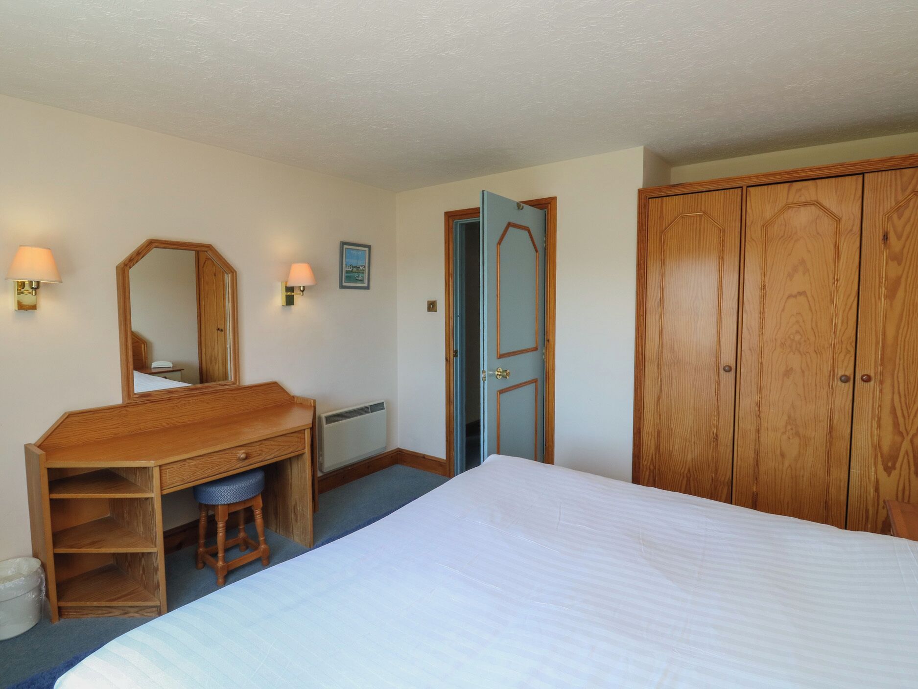 Hotelkamer met een bed, een houten bureau met stoel, een spiegel, twee wandlampen en een kledingkast.