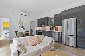 Uma sala de estar moderna com um sofá, uma área de jantar e uma cozinha com uma geladeira grande.