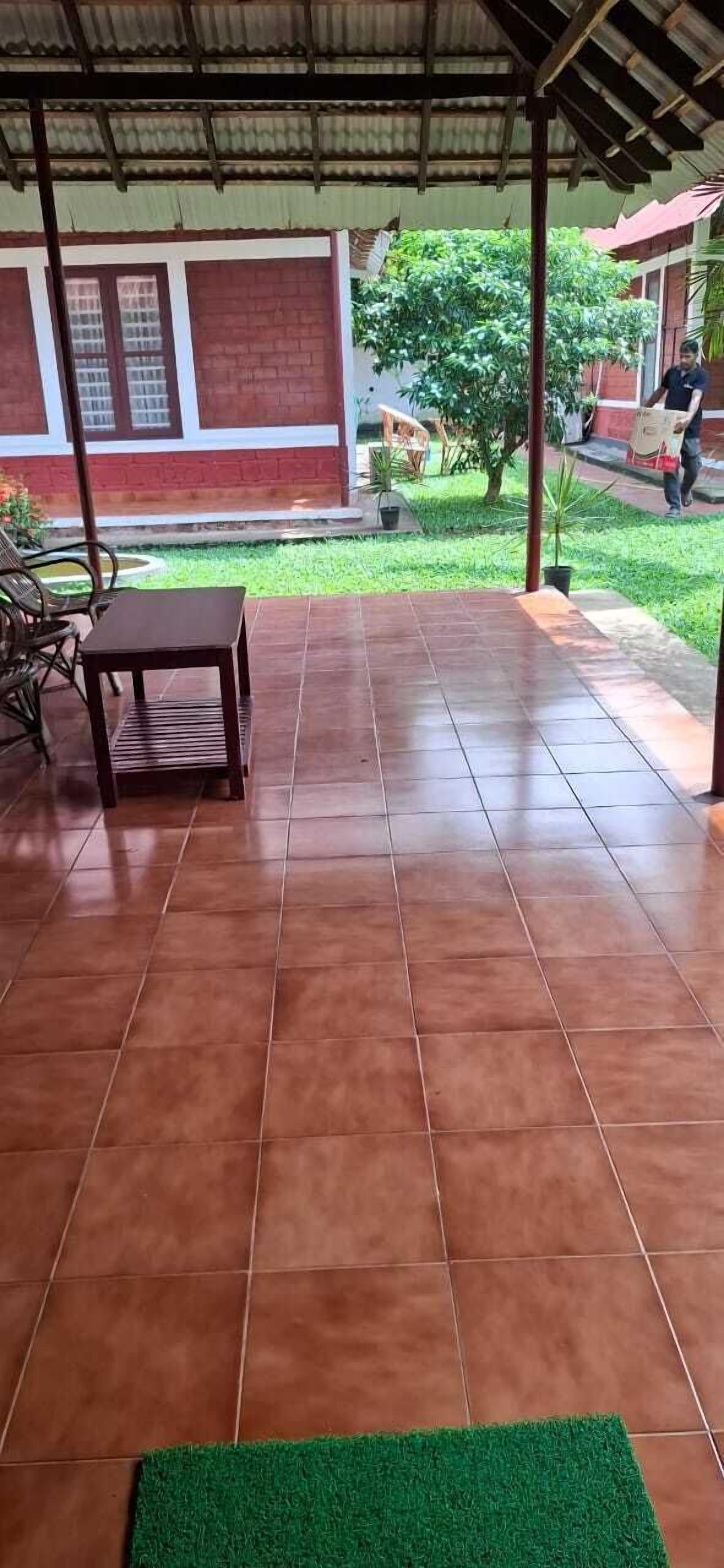 A covered patio area with tiled flooring, a wooden table, and a green mat.