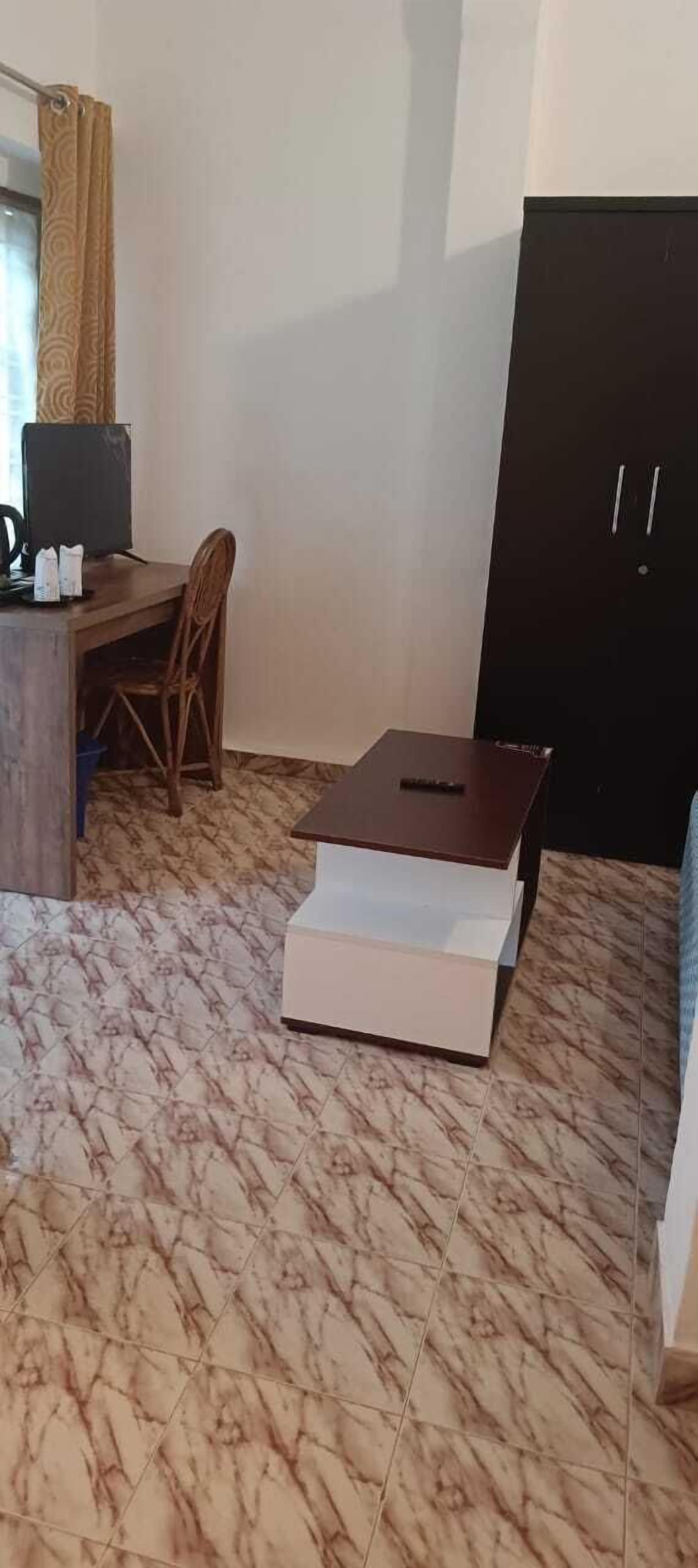 A room with a wooden desk, a chair, a television, a wardrobe, and a tiled floor.