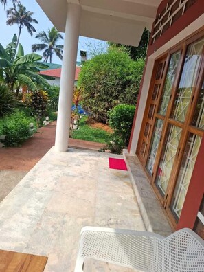 A covered outdoor area with a white chair, a red mat, and a variety of plants including palm trees and bushes. - hillview beach resort (Varkala)