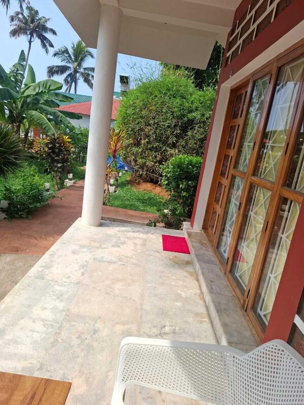 A covered outdoor area with a white chair, a red mat, and a variety of plants including palm trees and bushes. - hillview beach resort (Varkala)
