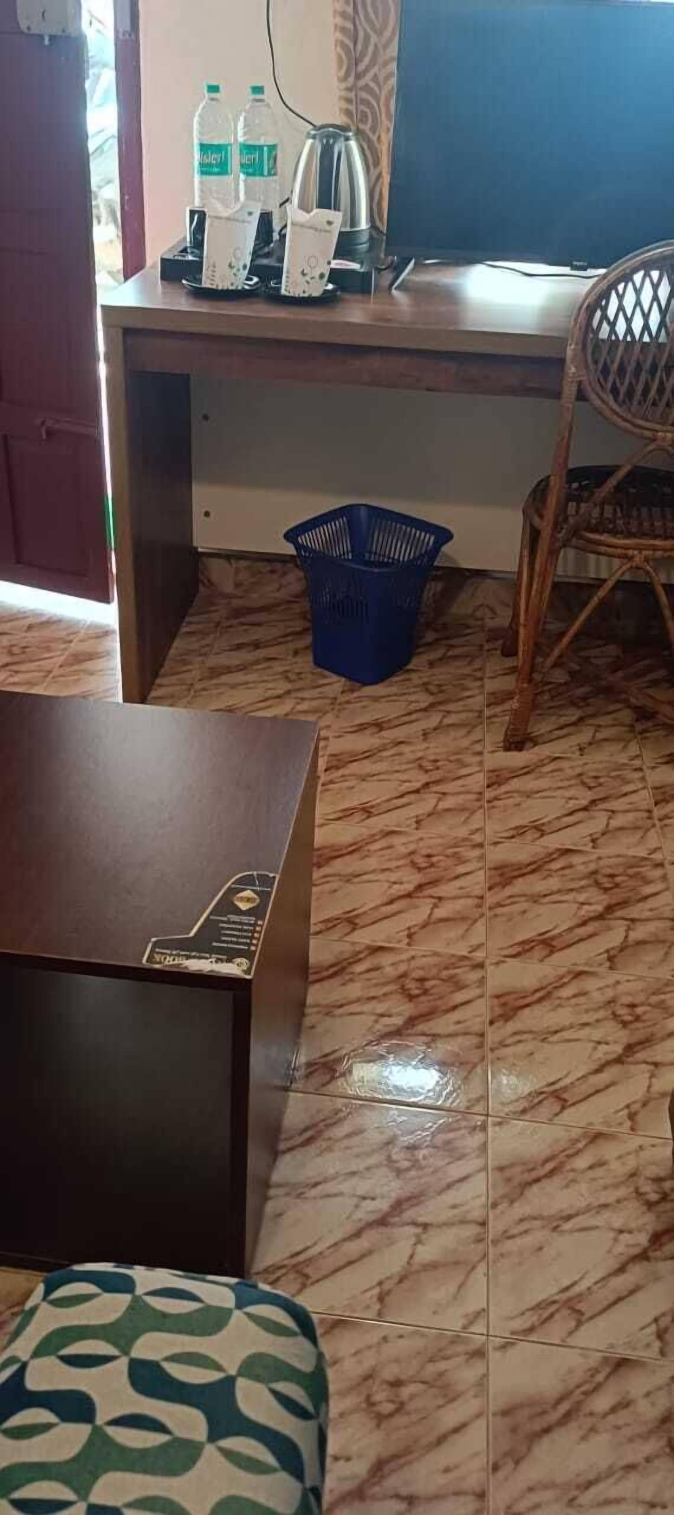 Una stanza con una scrivania, una sedia, un cesto blu e un pouf decorato.