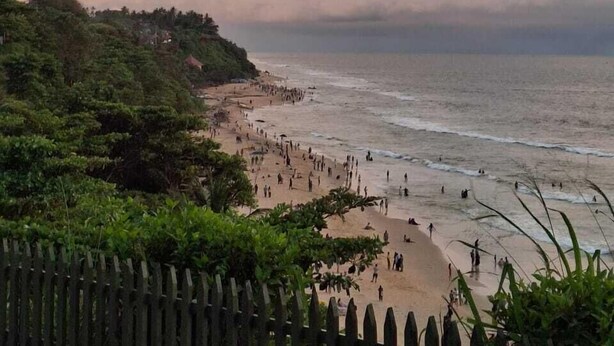 A beach with people, a wooden fence, and a cloudy sky. - hillview beach resort (Varkala)