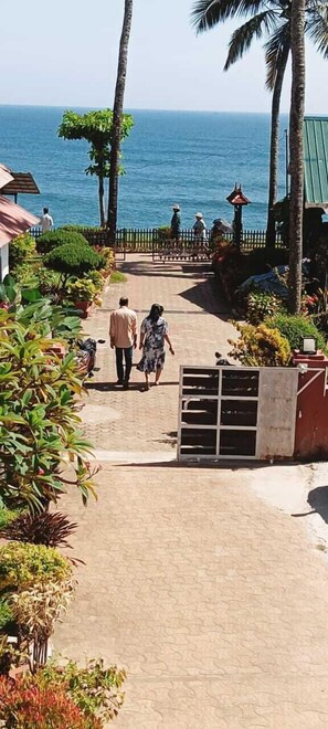 A pathway leading to a gate with palm trees and a view of the sea. - hillview beach resort (Varkala)