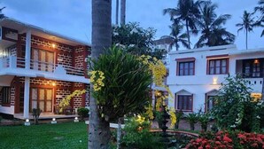 A two-story building with a balcony, surrounded by lush greenery and flowering plants. - hillview beach resort (Varkala)