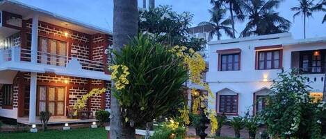 A two-story building with a balcony, surrounded by lush greenery and flowering plants.