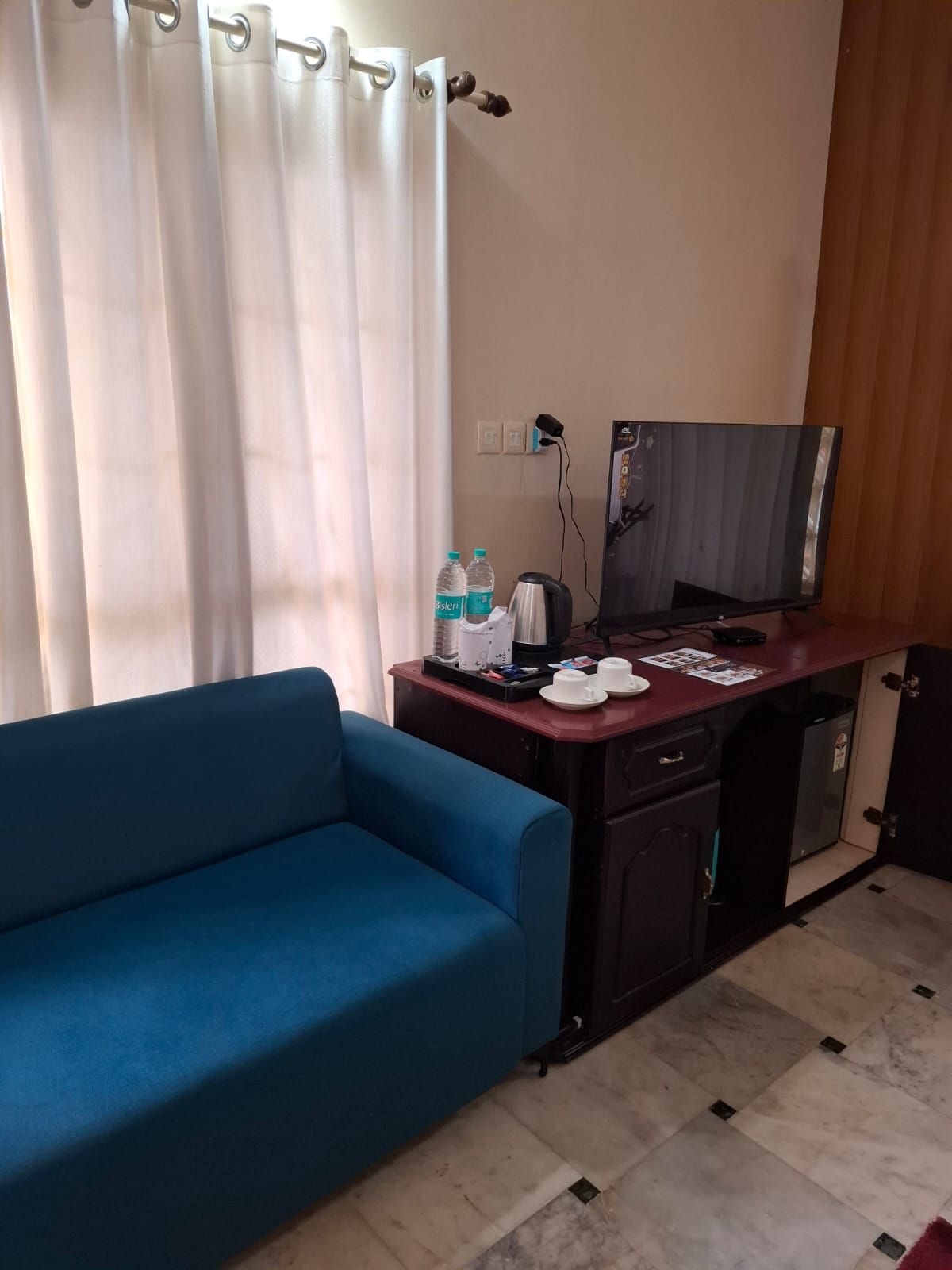 A room with a blue sofa, a desk with a coffee maker, water bottles, a television, and a cabinet.