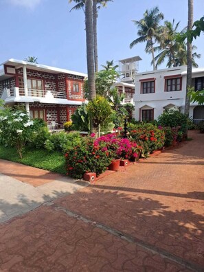 A two-story building with a balcony, surrounded by lush greenery and flowering plants. - hillview beach resort (Varkala)