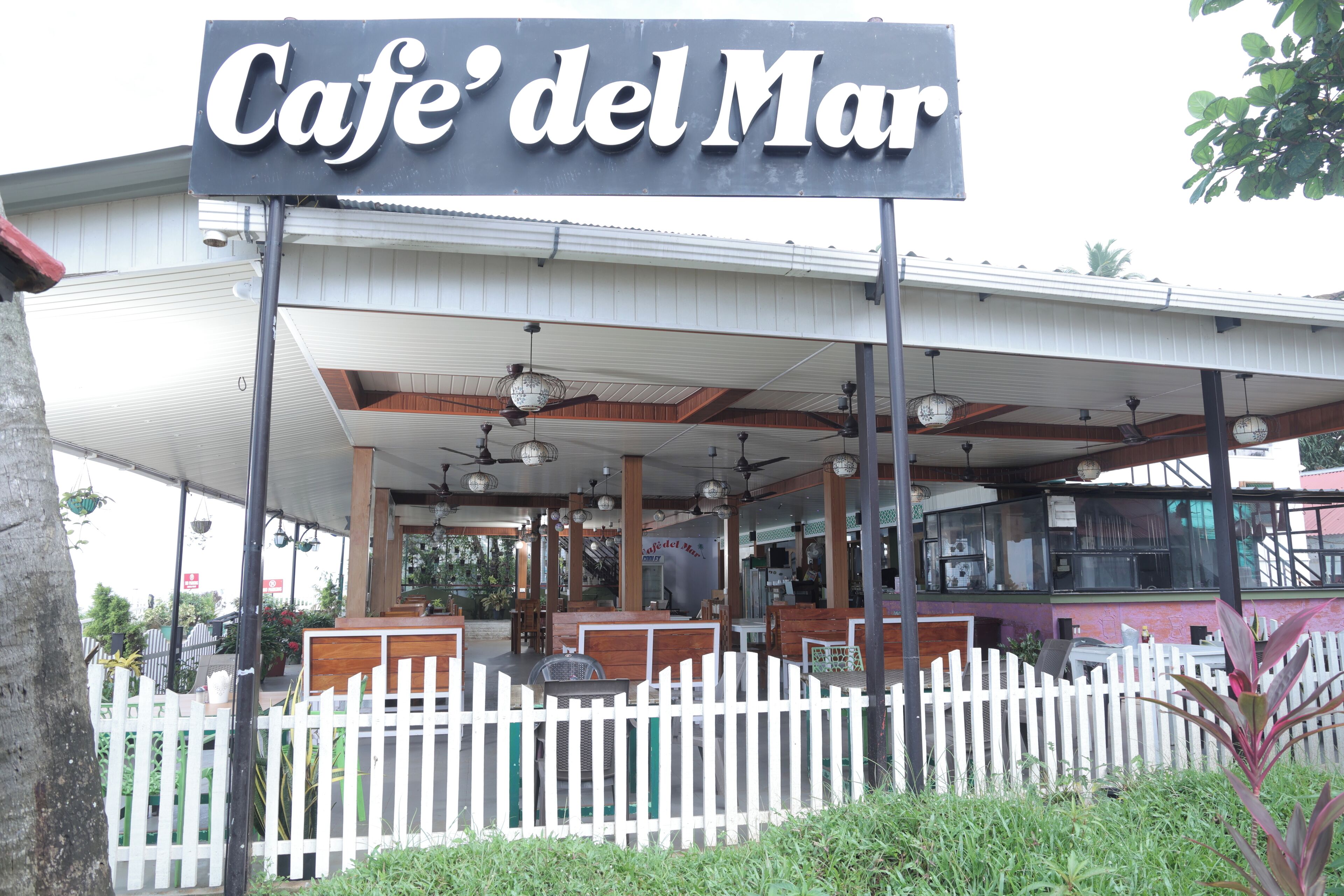 A cafe named Cafe del Mar with outdoor seating and a white picket fence.